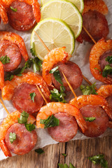 Delicious grilled shrimp with chorizo on skewers and herbs closeup on the table. vertical top view