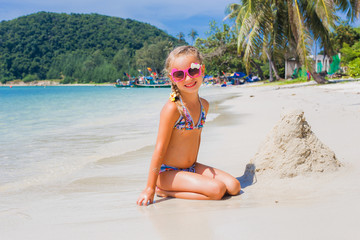 cute little girl in sunglasses and a swimsuit on the beach in paradise by the sea. Travel and...