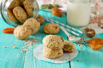 Healthy foods for breakfast. Homemade biscuits from oat flakes with sesame seeds, dried fruits, nuts in an open glass jar and milk on a wooden background. Healthy food concept.