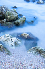 Sea wave and beach sand on a background of stones in a long exposure.