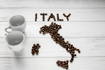 Map of the Italy made of roasted coffee beans laying on white wooden textured background with two coffee cups. Space for text