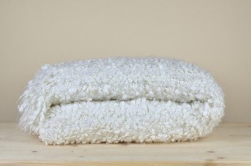 Folded white soft woolen blanket with cozy look on wooden shelf