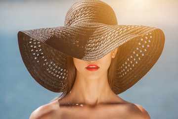 Attractive girl in a black hat worn on the head, on the beach. Close up of the face can be seen.