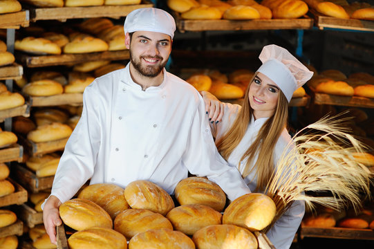 young man and woman in uniform bakers with spikelets of wheat in the hands on the background of the bakery
