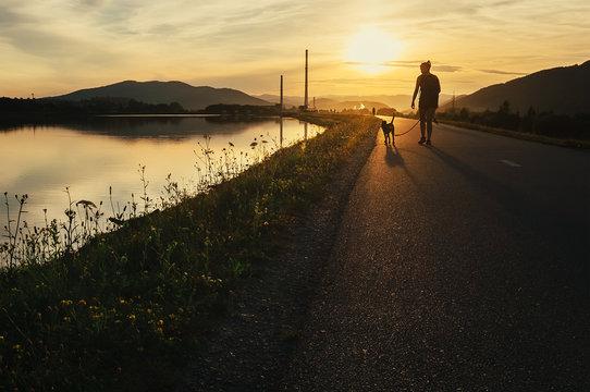 Woman walks with dog in sunset time