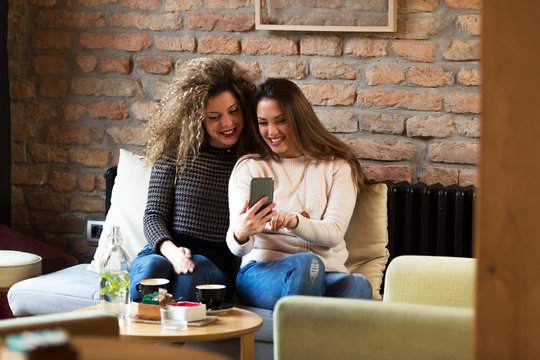 Two girls are smiling and using smart phone in a cafe