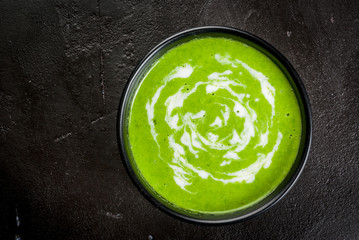 Summer diet light cream soup of green peas with yogurt and croutons, on black concrete stone background, copy space top view