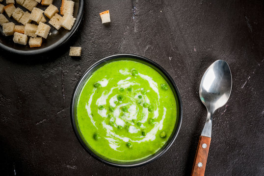 Summer diet light cream soup of green peas with yogurt and croutons, on black concrete stone background, copy space top view