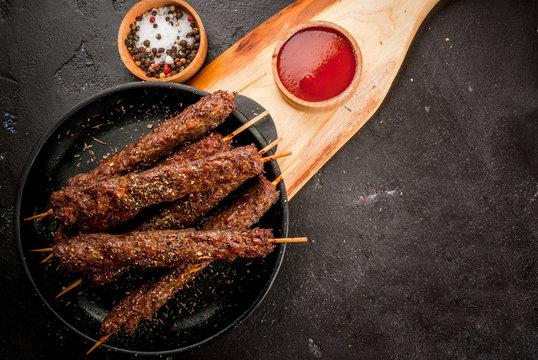 Shish kebab on a stick, from ground beef meat. Lula kebab, traditional Caucasian dish. On the black background of the concrete, on a chopping board, with ketchup, spices and tomatoes copy space above