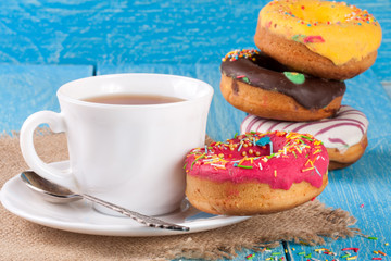 pile of glazed donuts with a cup of tea on a blue wooden background