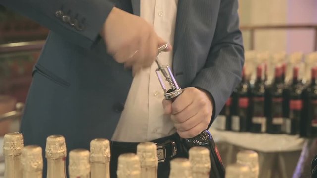 Picture of a young female bartender who is opening a bottle of wine with the corkscrew