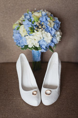 Bride`s wedding accessories: wedding shoes, rings and bouquet or boutonniere with delicate blue and white flowers 