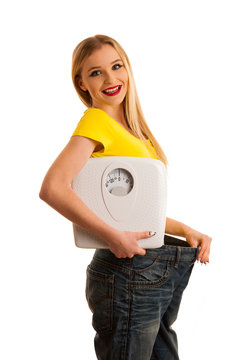 Happy womman holding a scale and too big trousers as she lost weight isolated over white background