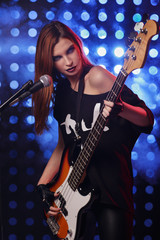 Beautiful girl with a guitar in the hands of performing on stage in a rock style