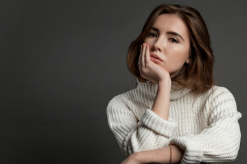 Girl model in white sweater on a gray background looking at the camera