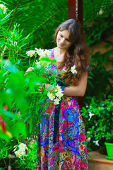 beautiful brunette woman in a colorful dress standing in the green garden among palm trees and flowers