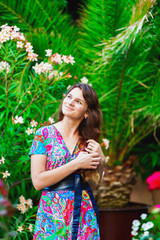 beautiful brunette woman in a colorful dress standing in the green garden among palm trees and flowers