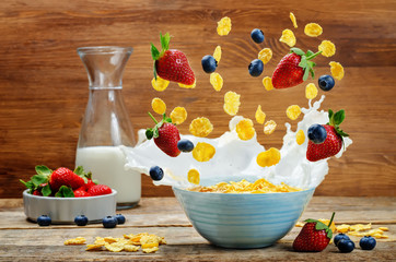 Healthy breakfast with milk, flying corn flakes, strawberries and blueberries