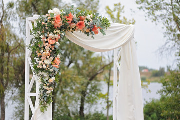 Beautiful wedding arch, decorated with white cloth and flowers, closeup