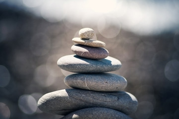 Tower of sea pebbles on blurred sunlight background.
