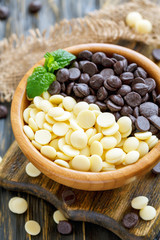 Drops of black and white chocolate in a wooden bowl.