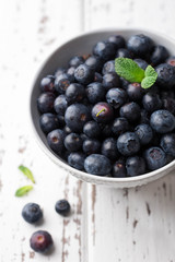 Fresh blueberries in bowl on light wooden background