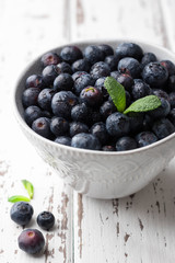 Fresh blueberries in bowl on light wooden background