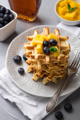 Stack of delicious homemade waffles with fresh fruit and berries on light background