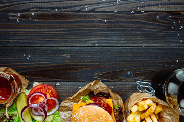 Fresh delicious burgers with french fries, sauce and drink on the wooden table top view, with copy...