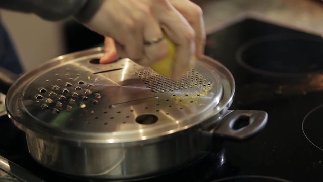 Close-up of chef hands grate a lemon on pan in restaurant kitchen