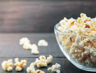 Glass bowl with freshly popped popcorn with salt on dark wooden background. Soft focus.