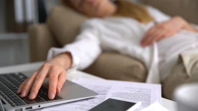 Tired young businesswoman sleeping on the couch in the office with laptop. Close-up of her hand on the keyboard. Dolly shot