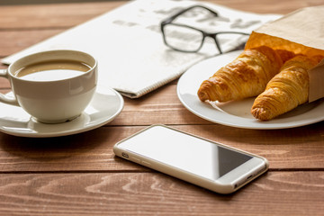 Business cup of coffee with croisant and phone on desk