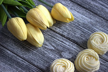 Spring flowers tulips with zephyr marshmallows on gray wooden background.