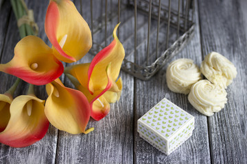 orange yellow calla lilies bouquet with marshmallow and cardboard box on a gray wooden background