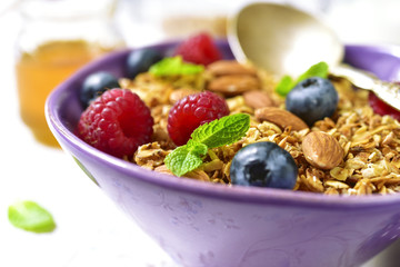 Homemade granola with fresh berry for a breakfast in a purple bowl.