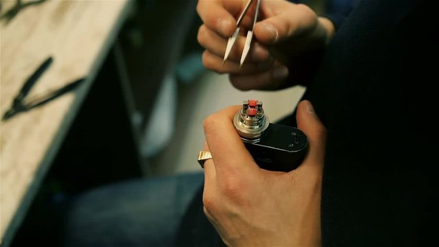 Male hands regulate electronic cigarette coils. After-sales service of the e-cigarette. Glowing spiral
for background. ENDS.
