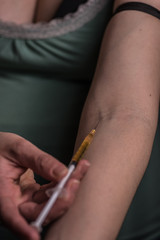 woman holding needle next to vein in arm, getting ready to shoot up, drugs, heroin