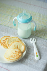 pancakes with cottage cheese on a light dish with a bottle for feeding the baby. Breakfast for the child