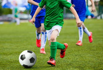 Obraz premium Young Boys Kids Children Playing Football Soccer Game. Running Soccer Players in Green and Blue Uniforms. Boys Kicking Soccer Ball