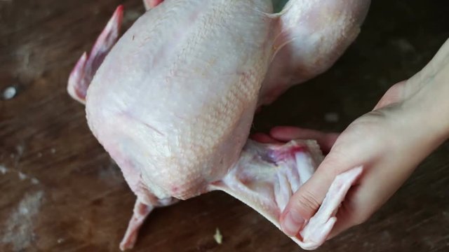 Hands preparing whole raw chicken on a wooden cooking board