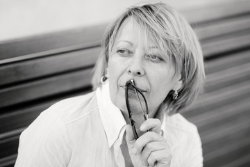 Portrait of pensive Mature woman with glasses in hands, black and white photo.