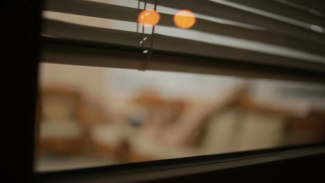 somebody spying on a girl from the street through the window blinds . crime