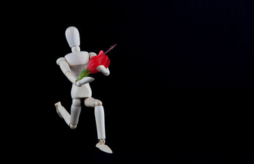 Wooden figurine kneeling with flower on black background with copy space. Wedding, engagement,...