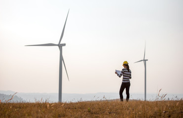 Woman engineer or architect with white safety hat and wind turbines on background
