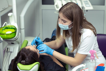 Dentist at work examining brunette woman's teeth in dental clinic