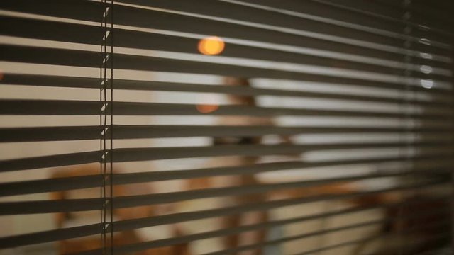 somebody spying on a girl from the street through the window blinds . crime