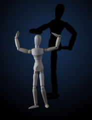 Wooden figurine flexing muscles in bodybuilder pose with shadow showing a different pose on dark...