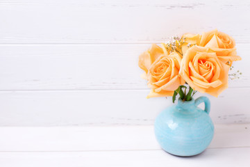 Peach color roses flowers in blue vase on white wooden background.