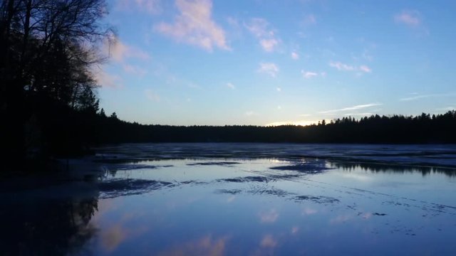 Mirroring lake sunset, Pan time lapse of evening sky clouds mirroring on a icy lake, in siikajärvi, of Nuuksio national park, in Finland